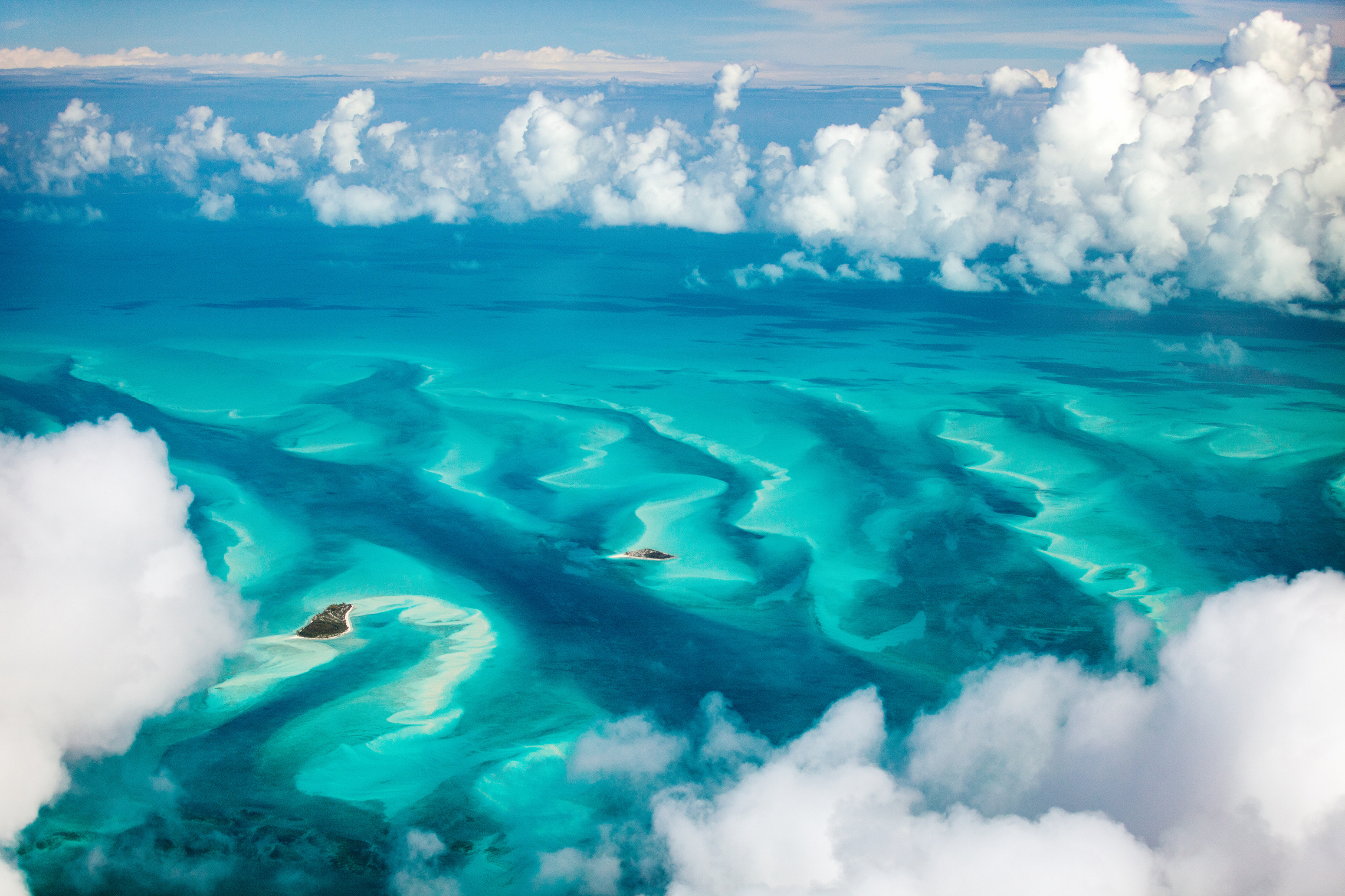 Aerial view of a turquoise sea below clouds_Adobestock